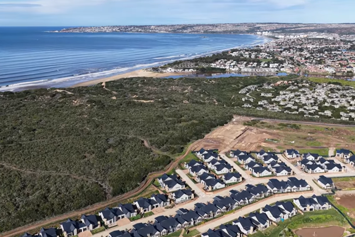 Aerial view of a coastal residential estate development featuring modern homes, paved roads, and proximity to the ocean and natural landscape.