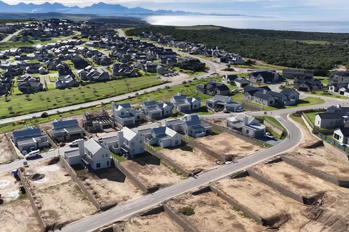 An aerial view of a modern residential estate development featuring newly constructed homes, paved streets, and scenic coastal surroundings.