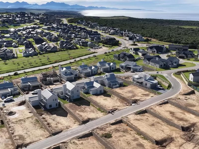 An aerial view of a modern residential estate development featuring newly constructed homes, paved streets, and scenic coastal surroundings.