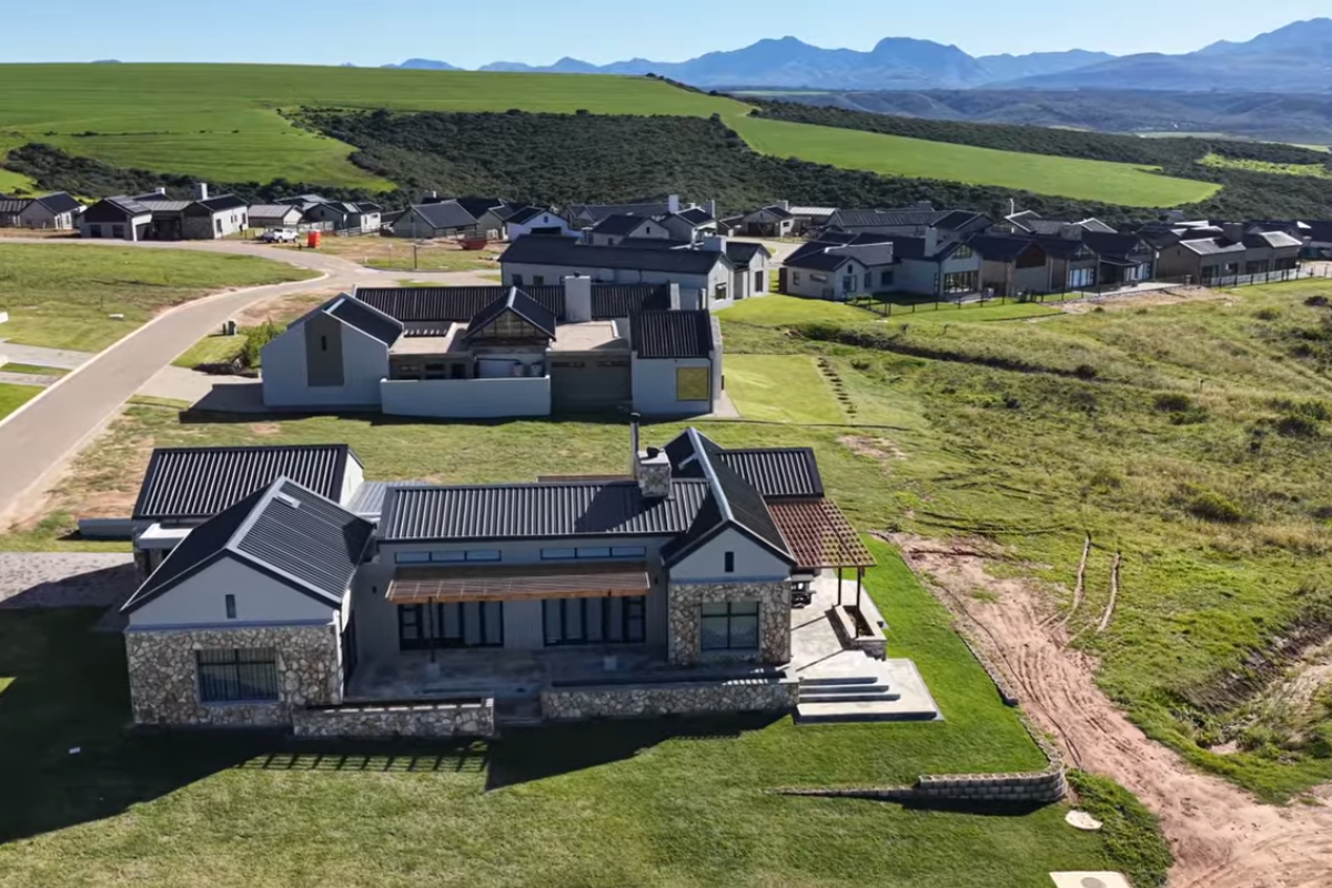 Aerial view of a modern residential property featuring stone cladding, metal roofing, and a timber pergola, situated within a scenic estate landscape.