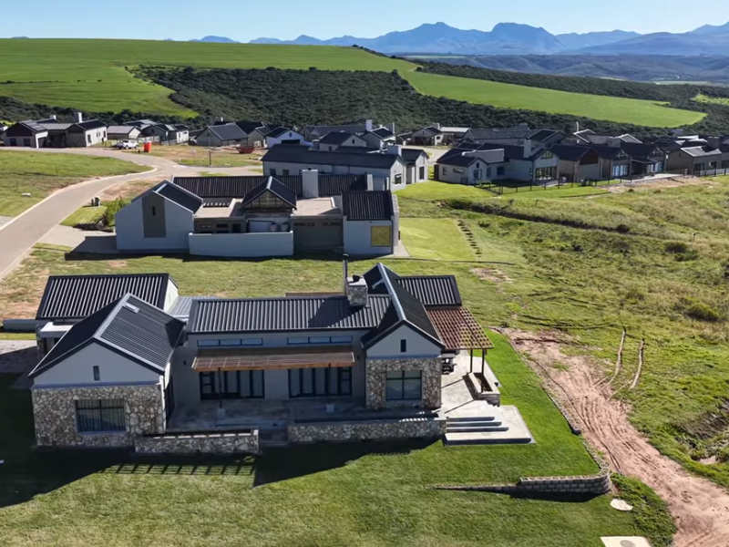 Aerial view of a modern residential property featuring stone cladding, metal roofing, and a timber pergola, situated within a scenic estate landscape.
