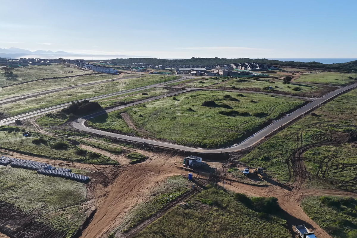 Aerial view of a developing residential estate featuring paved road infrastructure, security access point, and surrounding coastal landscape.
