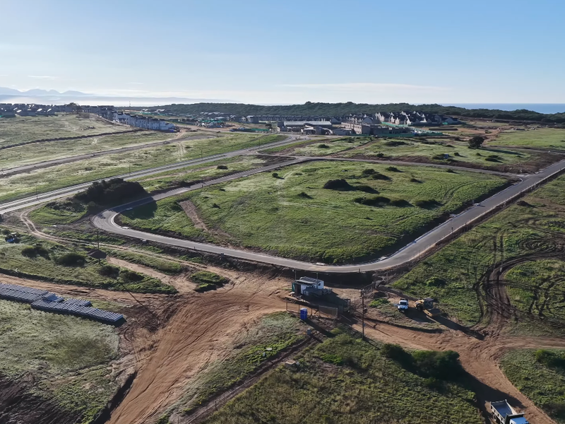 Aerial view of a developing residential estate featuring paved road infrastructure, security access point, and surrounding coastal landscape.