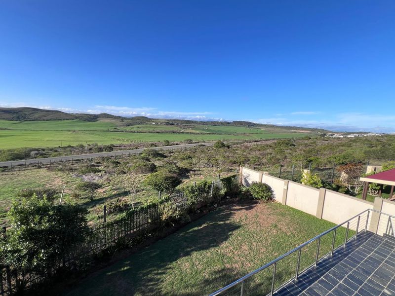 Elevated view overlooking a landscaped garden, perimeter wall, and expansive green rural landscape under a clear blue sky.