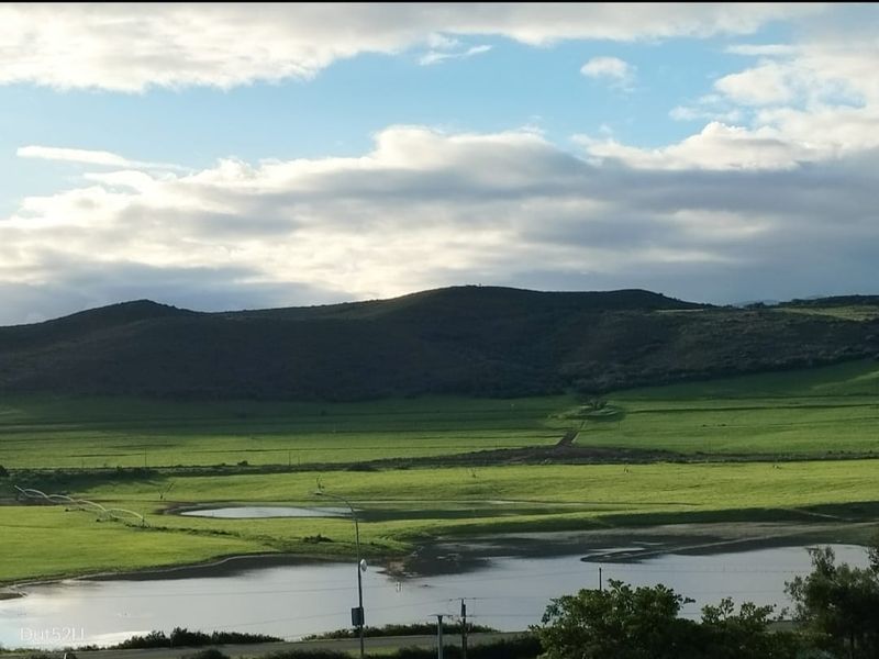 A scenic view of rolling green hills, open fields, and a small body of water under a cloudy sky.