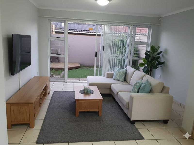 A bright living room featuring tiled flooring and a large sliding glass door that provides direct access to the rear garden area.