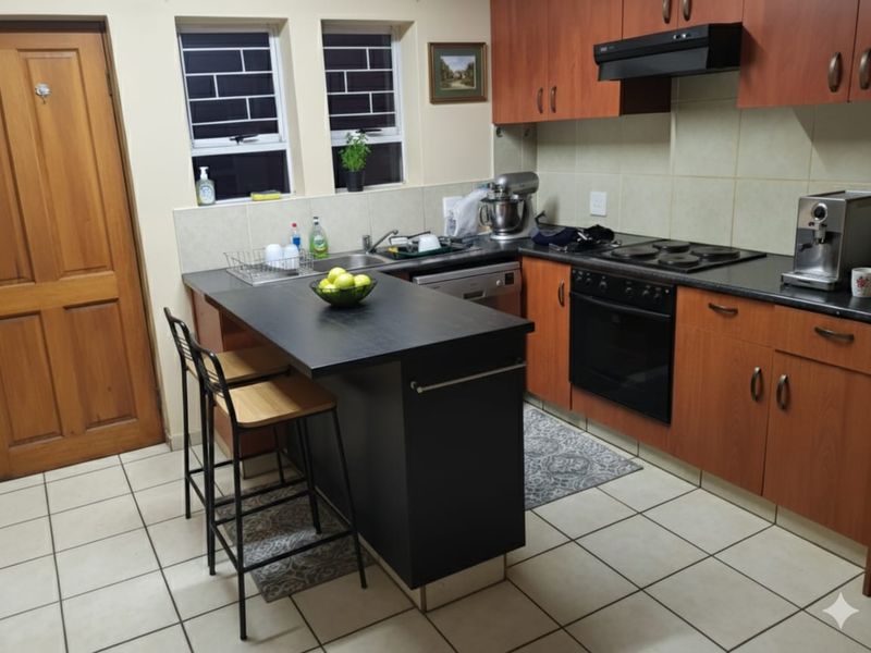 A functional kitchen featuring wood-tone cabinetry, a central island, built-in oven, electric hob, and tiled flooring with practical workspace.