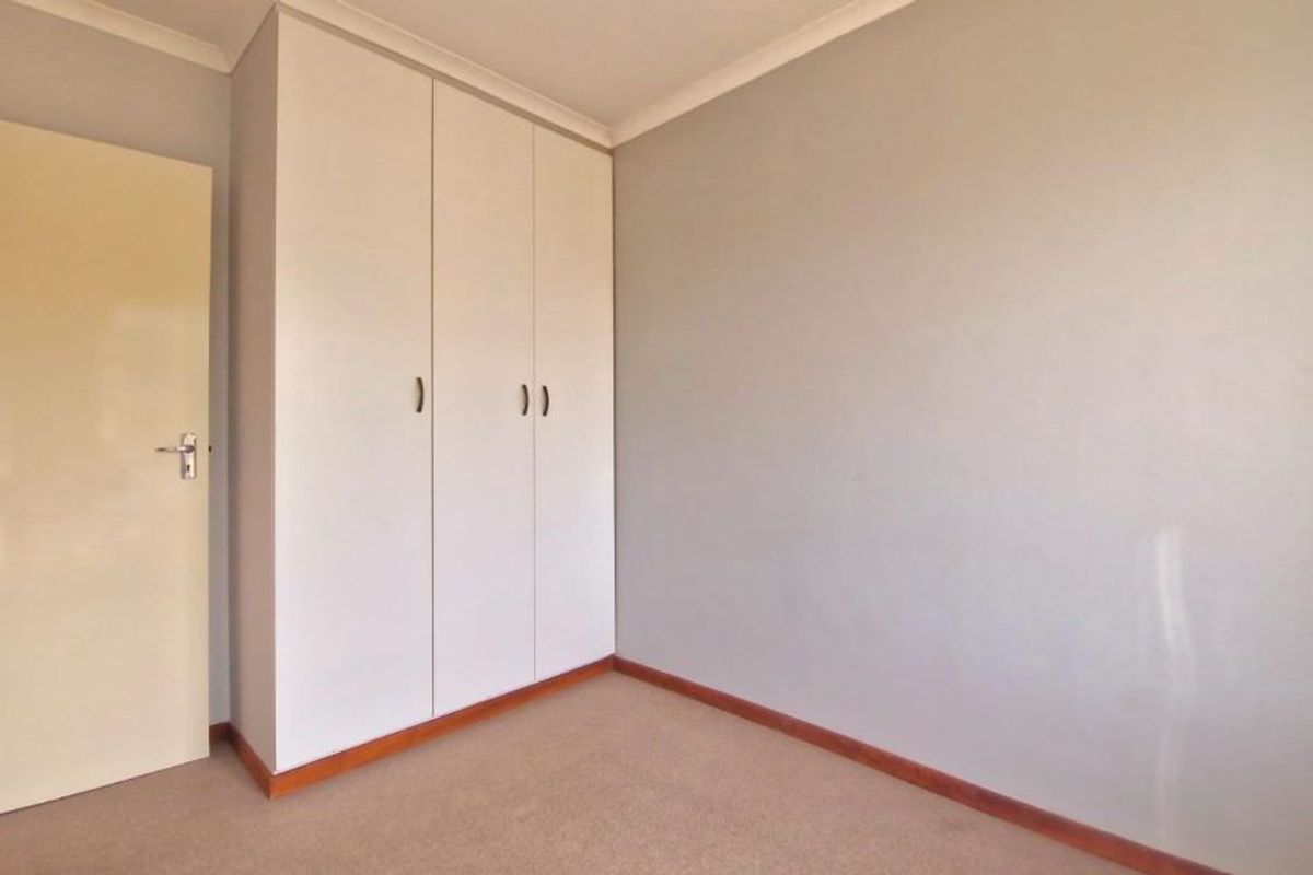 A clean, empty bedroom featuring neutral wall tones, carpeted flooring, and a built-in wardrobe with white cabinetry.