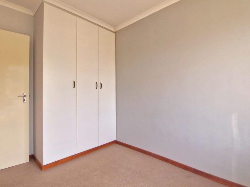 A clean, empty bedroom featuring neutral wall tones, carpeted flooring, and a built-in wardrobe with white cabinetry.