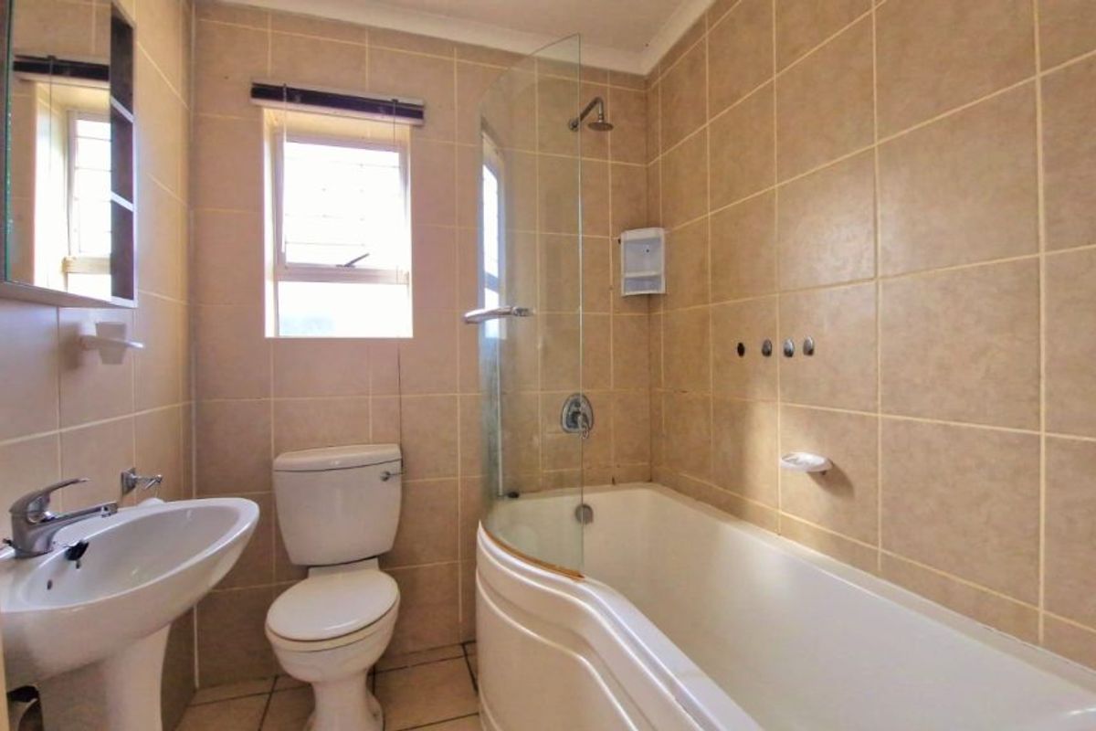 A functional bathroom featuring a pedestal basin, toilet, and a bathtub with an integrated shower and glass screen, finished with neutral wall tiles.
