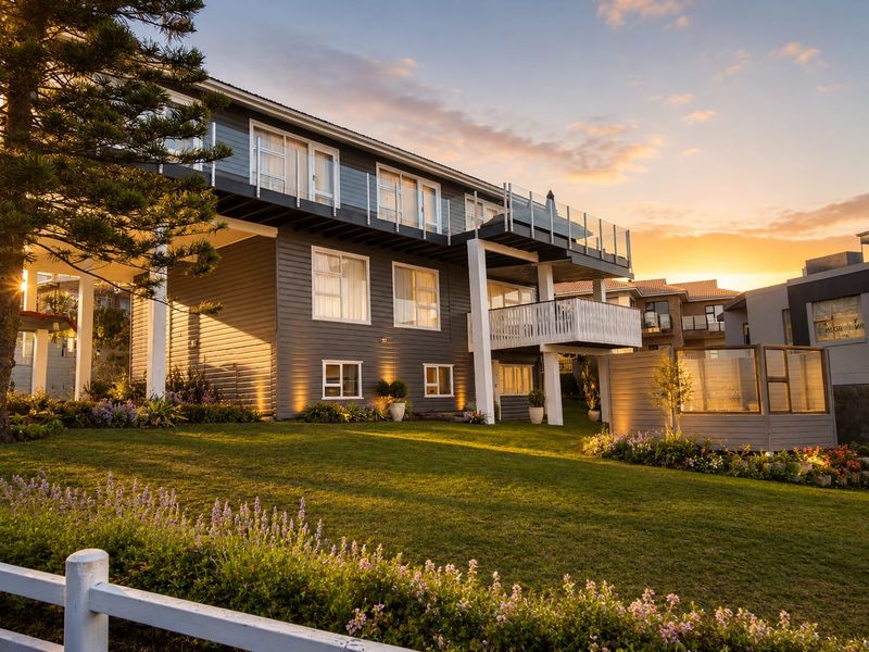 A beautifully maintained rear exterior view of a multi-level home featuring timber cladding, a spacious balcony with glass balustrades, and a manicured garden.
