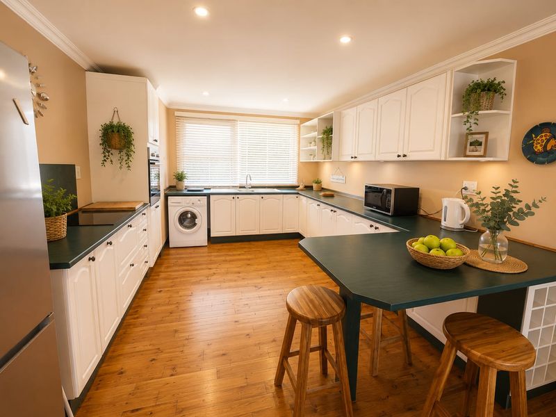 A well-maintained kitchen featuring white cabinetry, dark countertops, integrated appliances, and warm wood-look flooring with ample natural light.