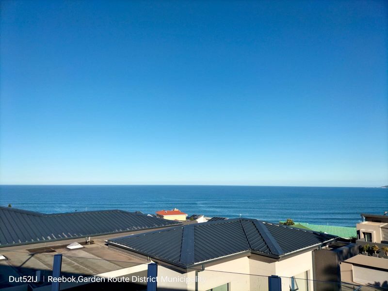 An elevated view overlooking the ocean, featuring modern metal roofing and a glass balustrade in the foreground.