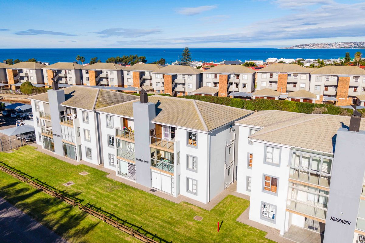 Aerial view of a multi-story apartment complex featuring tiled roofs, private balconies, and well-maintained communal lawns with ocean views in the background.