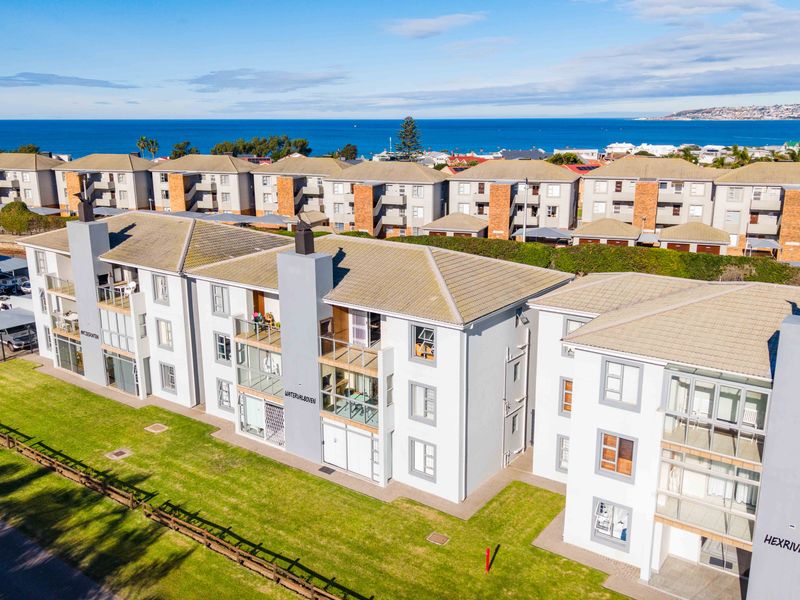 Aerial view of a multi-story apartment complex featuring tiled roofs, private balconies, and well-maintained communal lawns with ocean views in the background.