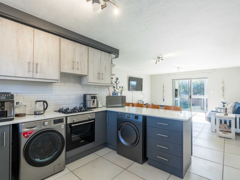 Modern open-plan kitchen featuring two-tone cabinetry, stone countertops, subway tile backsplash, and integrated appliances, flowing into a bright living area with garden access.