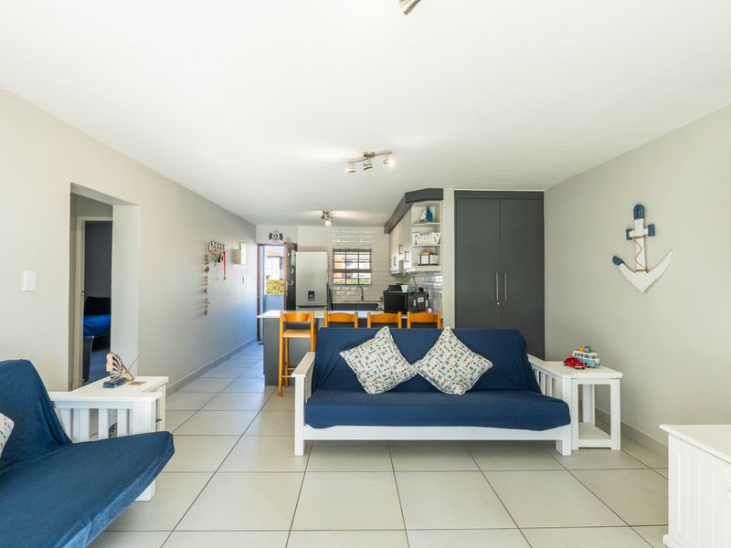An open-plan living and kitchen area featuring neutral tiled flooring, modern cabinetry, and a functional kitchen island with breakfast bar seating.