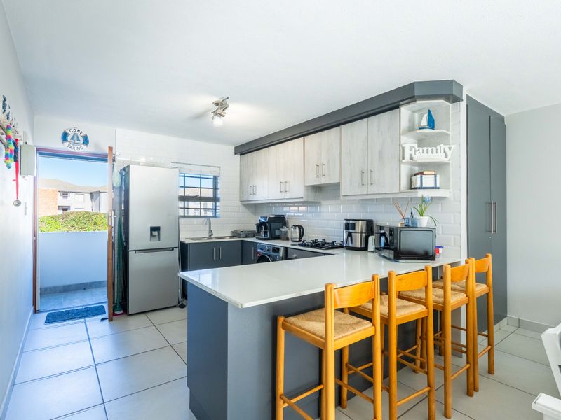 Modern kitchen featuring two-tone cabinetry, stone countertops, a breakfast bar, and subway tile backsplash, with direct access to an outdoor balcony area.