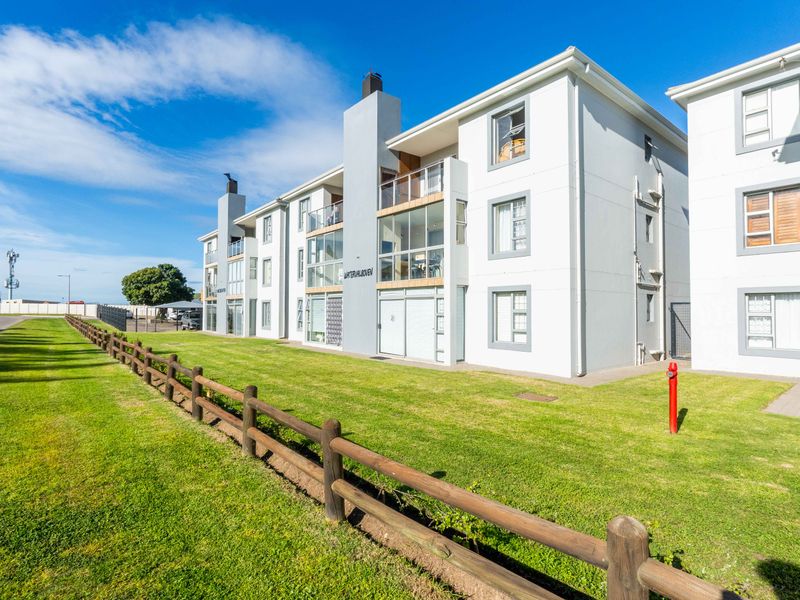 Exterior view of a modern apartment complex featuring white facade, balconies, and well-maintained surrounding lawn area with timber fencing.