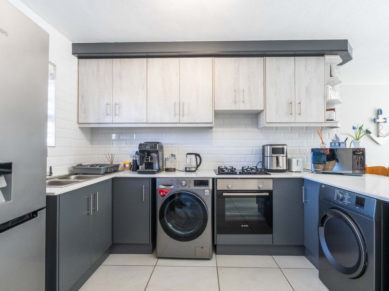 Modern kitchen featuring two-tone cabinetry, subway tile backsplash, stone countertops, integrated gas hob, and built-in oven with tiled flooring.