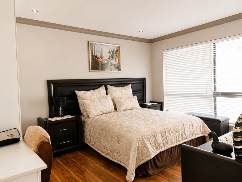 A well-maintained bedroom featuring timber laminate flooring, recessed downlighting, crown molding, and large windows fitted with venetian blinds.