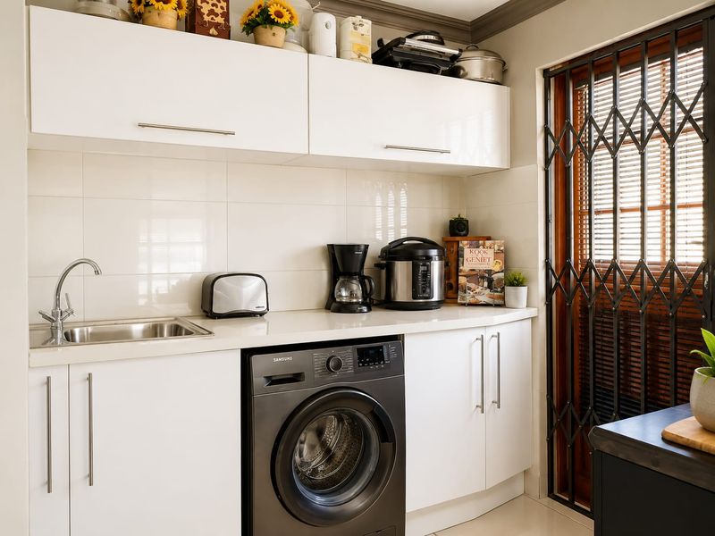 A clean and functional laundry area featuring white built-in cabinetry, a stainless steel sink, and a secure metal gate.