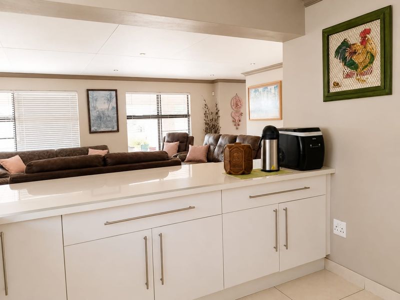 Open plan kitchen and living area featuring modern white cabinetry, quartz countertops, tiled flooring, and recessed lighting with a seamless flow to the lounge.