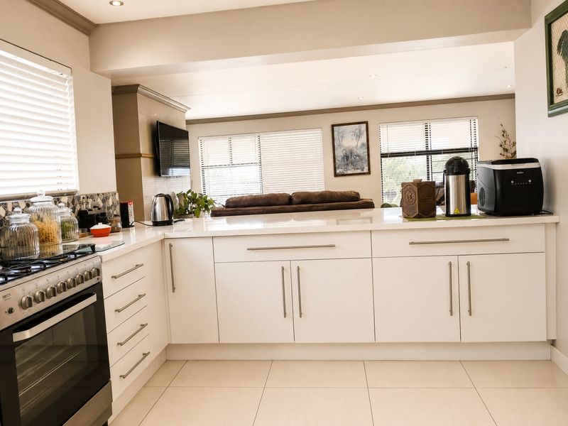 Modern open-plan kitchen featuring white cabinetry, quartz countertops, and a gas stove, seamlessly flowing into the adjacent living area with tiled flooring throughout.