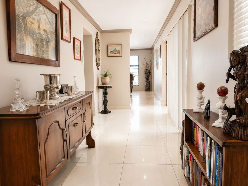 A bright and spacious hallway featuring polished tiled flooring, recessed downlighting, and elegant coved cornicing, providing a clean and well-maintained transition between living areas.