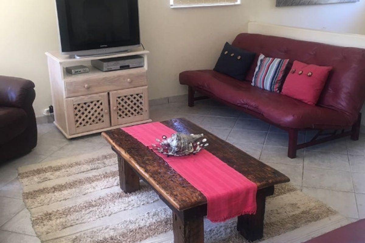 A living room featuring tiled flooring, a wall-mounted air conditioning unit, and a window with vertical blinds.