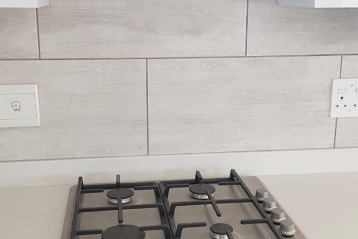 Modern kitchen featuring a built-in stainless steel gas hob, oven, and extractor fan with contemporary tiled splashback and white cabinetry.