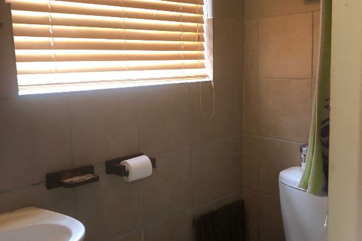 A compact bathroom featuring tiled walls, a pedestal basin, and a toilet with a wooden seat.