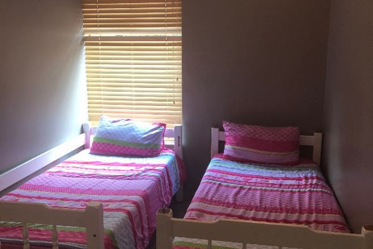 A bedroom featuring tiled flooring, a wall-mounted air conditioning unit, and wooden venetian blinds.