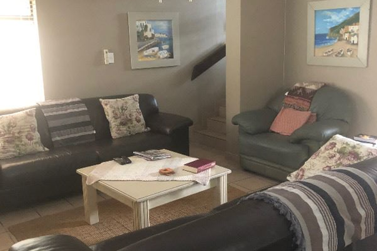 A comfortable living room featuring a ceiling fan, wall-mounted air conditioning unit, and tiled flooring.
