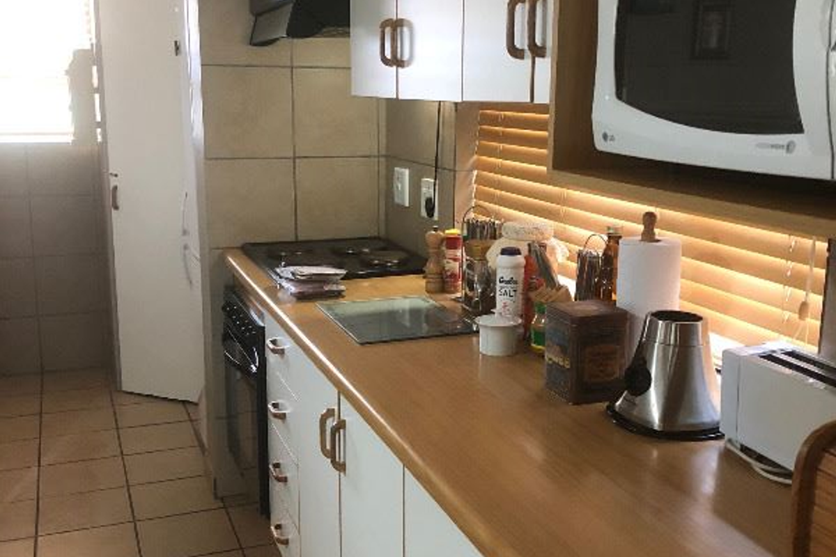 A functional galley-style kitchen featuring white cabinetry, laminate countertops, a built-in oven, and a hob with an extractor fan.