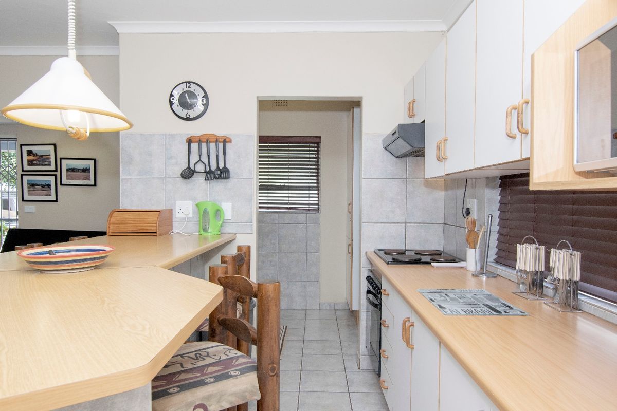 A functional kitchen featuring light-toned cabinetry, a breakfast bar, tiled splashbacks, and built-in cooking appliances, with an adjacent scullery area.