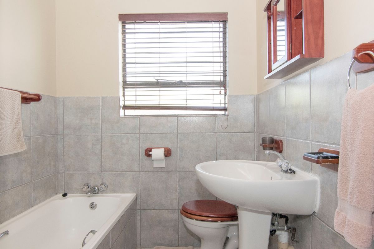 A functional bathroom featuring a bathtub, pedestal basin, and tiled walls with a window for natural light.