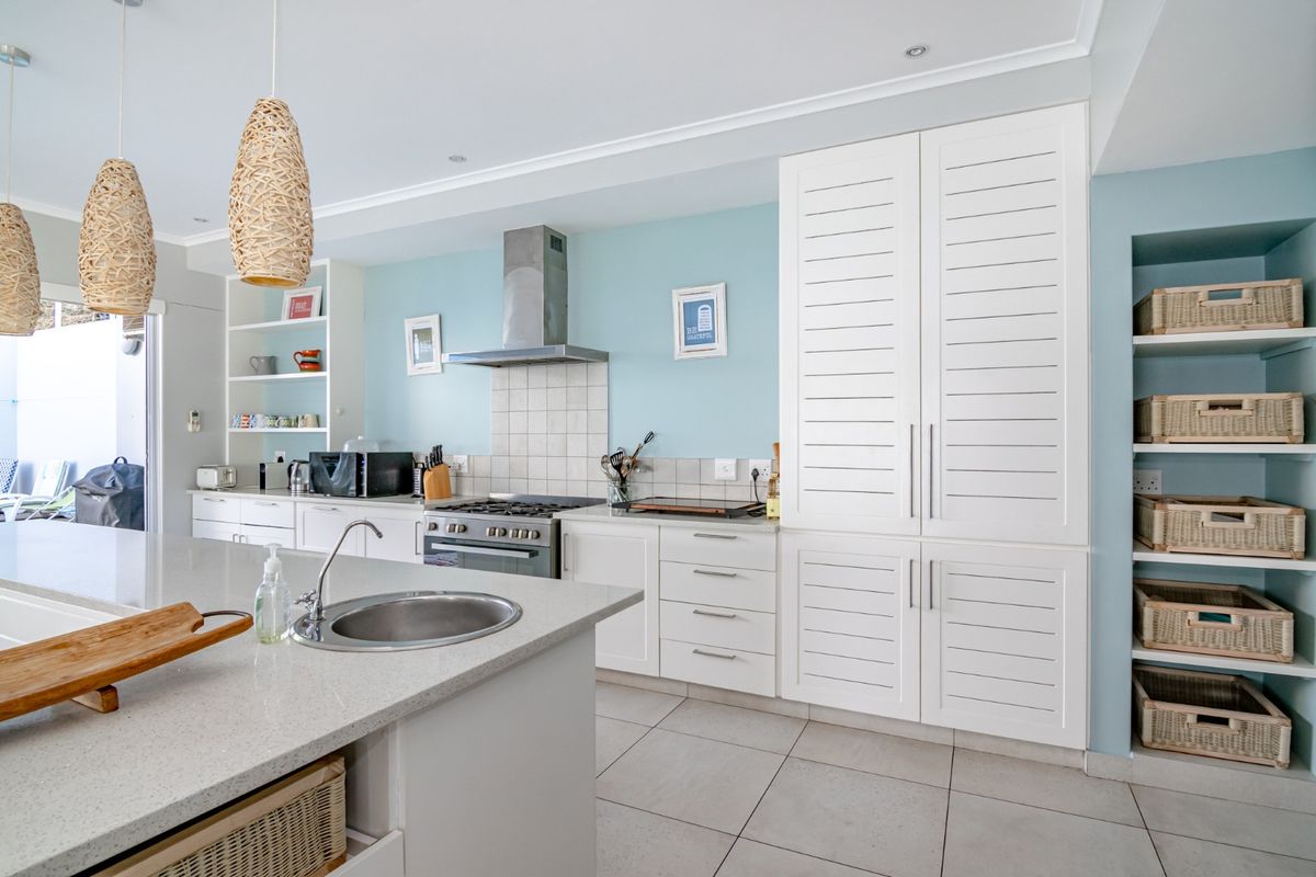 Modern kitchen featuring white cabinetry, stone countertops, a central island with a prep sink, stainless steel gas stove, and built-in pantry storage.