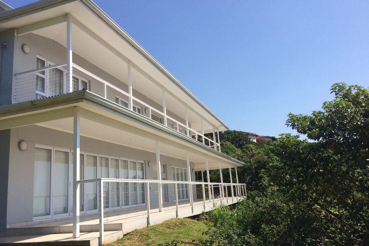 A two-story residential building featuring expansive covered balconies on both levels, providing outdoor living space with views of the surrounding greenery.