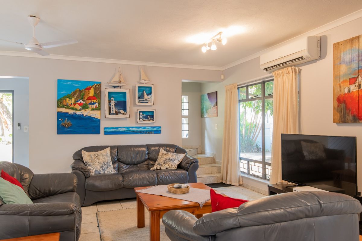 A comfortable living room featuring tiled flooring, a wall-mounted air conditioning unit, ceiling fan, and large windows providing natural light.