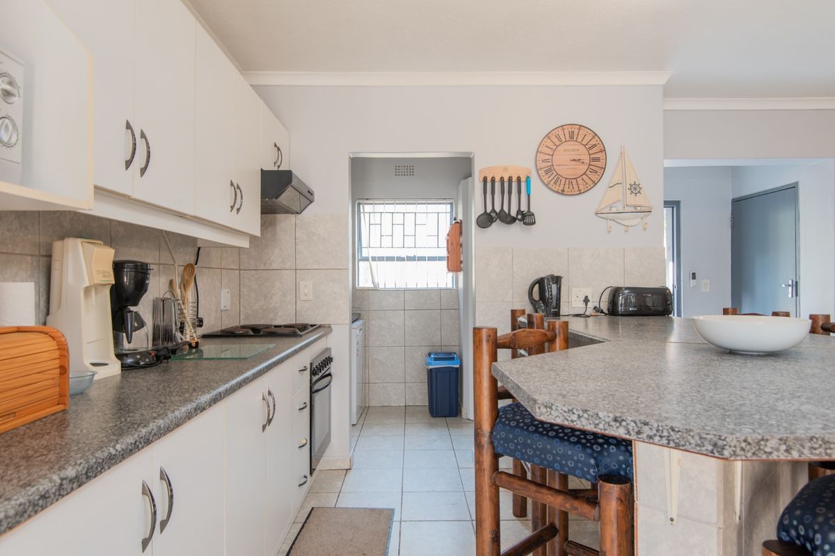 A functional kitchen featuring white cabinetry, granite-look countertops, a built-in oven and hob, and an adjoining scullery area with tiled flooring.
