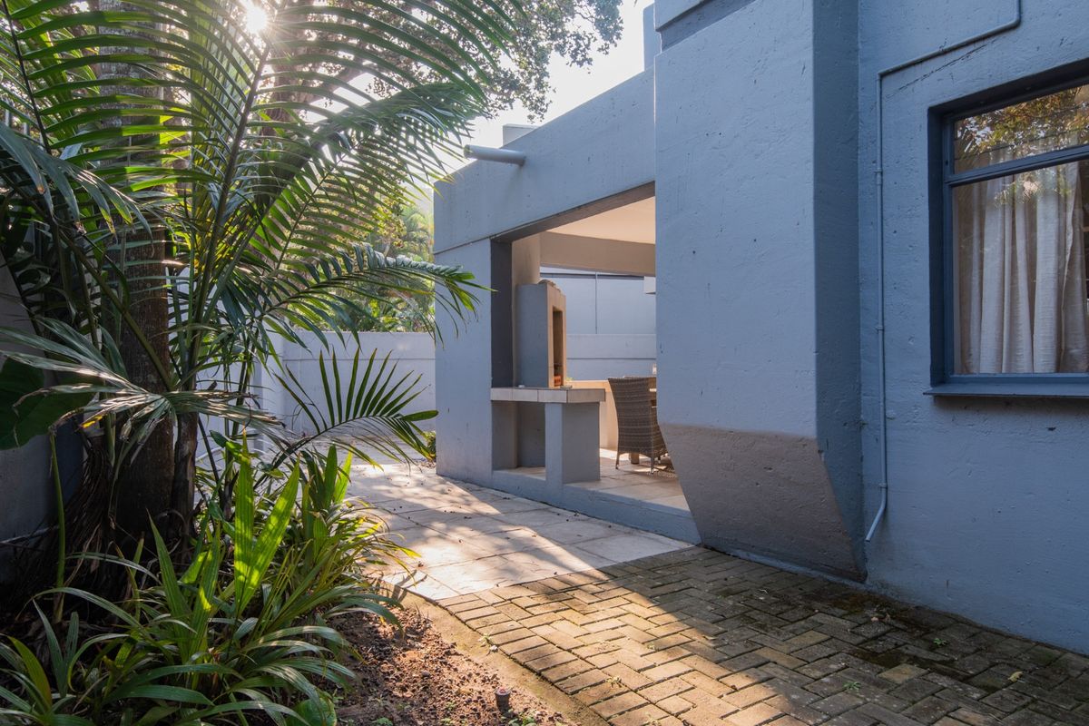 A view of the rear exterior featuring a paved patio area with a built-in braai, surrounded by landscaped garden elements.