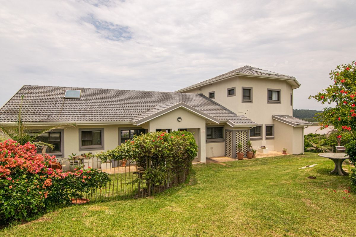 Rear view of a multi-level residential property featuring a tiled roof, skylight, and a spacious garden with a paved patio area.