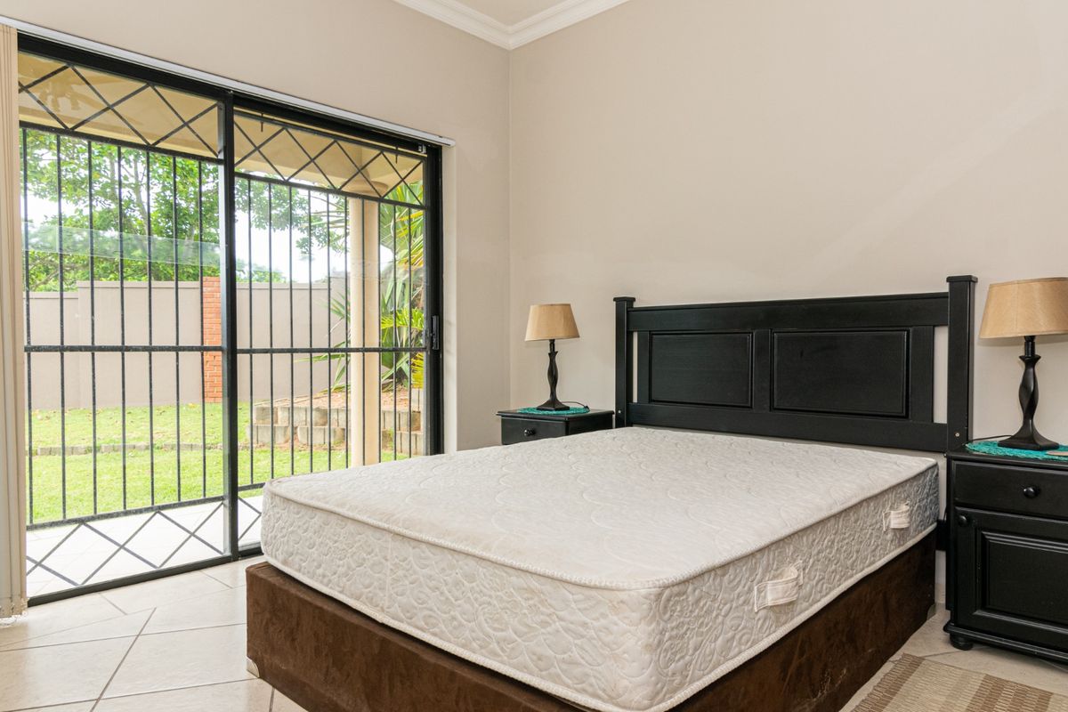 A well-lit bedroom featuring tiled flooring and a sliding glass door with security gate providing direct access to the garden area.