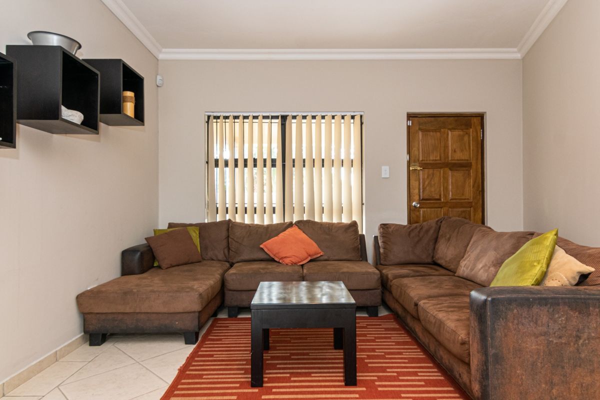 A living room featuring tiled flooring, vertical blinds, and a solid wood door, providing a functional space with neutral wall tones.