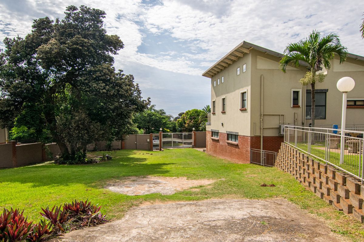 A view of the rear garden area featuring a brick retaining wall, metal fencing, and a spacious lawn adjacent to the property's exterior.