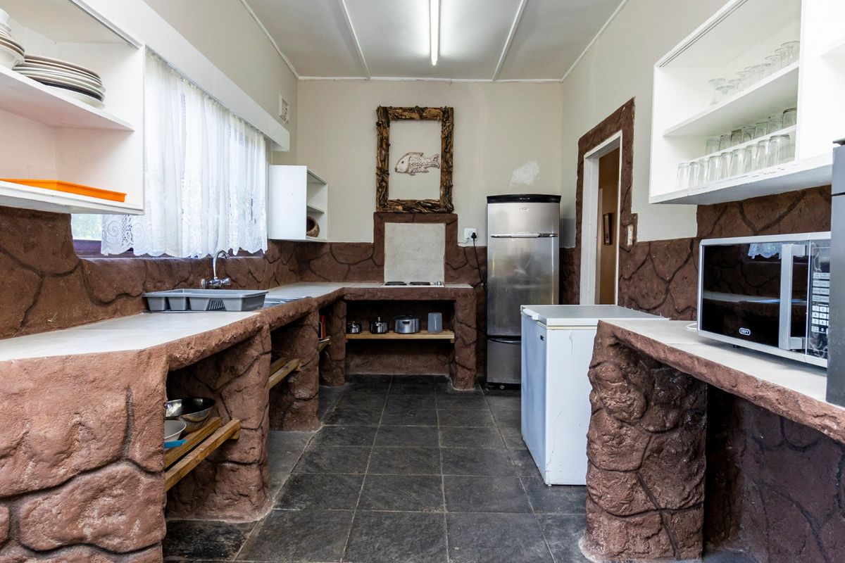 A rustic kitchen featuring custom masonry-style stone counters, dark tiled flooring, and open shelving, offering a unique, dated aesthetic.