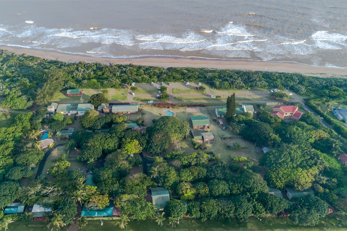 An aerial view of a coastal property complex featuring multiple buildings, lush green landscaping, and proximity to the beach.