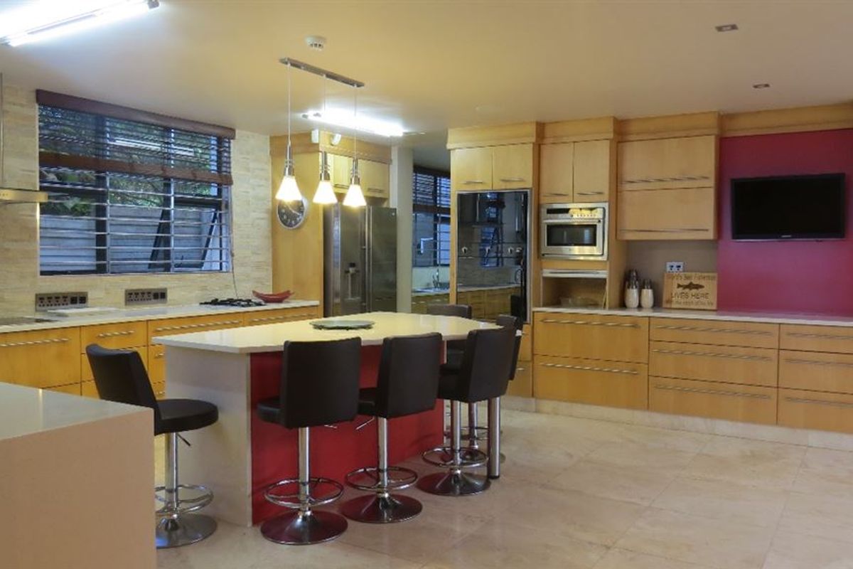 Spacious kitchen featuring a central island with breakfast bar seating, light wood cabinetry, stone countertops, and integrated appliances.