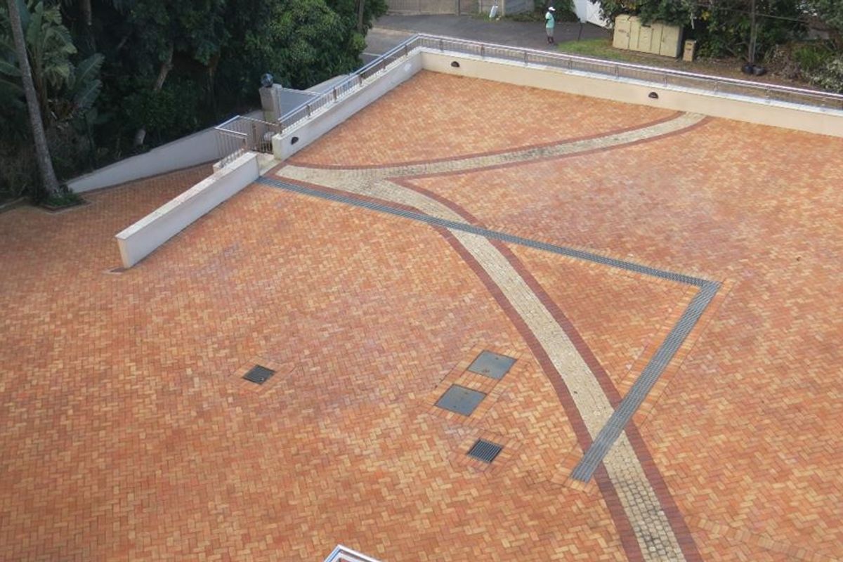 A spacious paved outdoor courtyard area featuring decorative brick patterns, retaining walls, and integrated drainage systems.